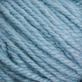 Close-up image of thick, soft, light blue Halcyon Deco Rug Wool by Caledonian Dye Works. The yarn strands are twisted together, showcasing a fluffy and slightly fuzzy texture. Made from 100% wool, the color and texture are consistent throughout the image, highlighting the material's snug and cozy appearance perfect for versatile projects.