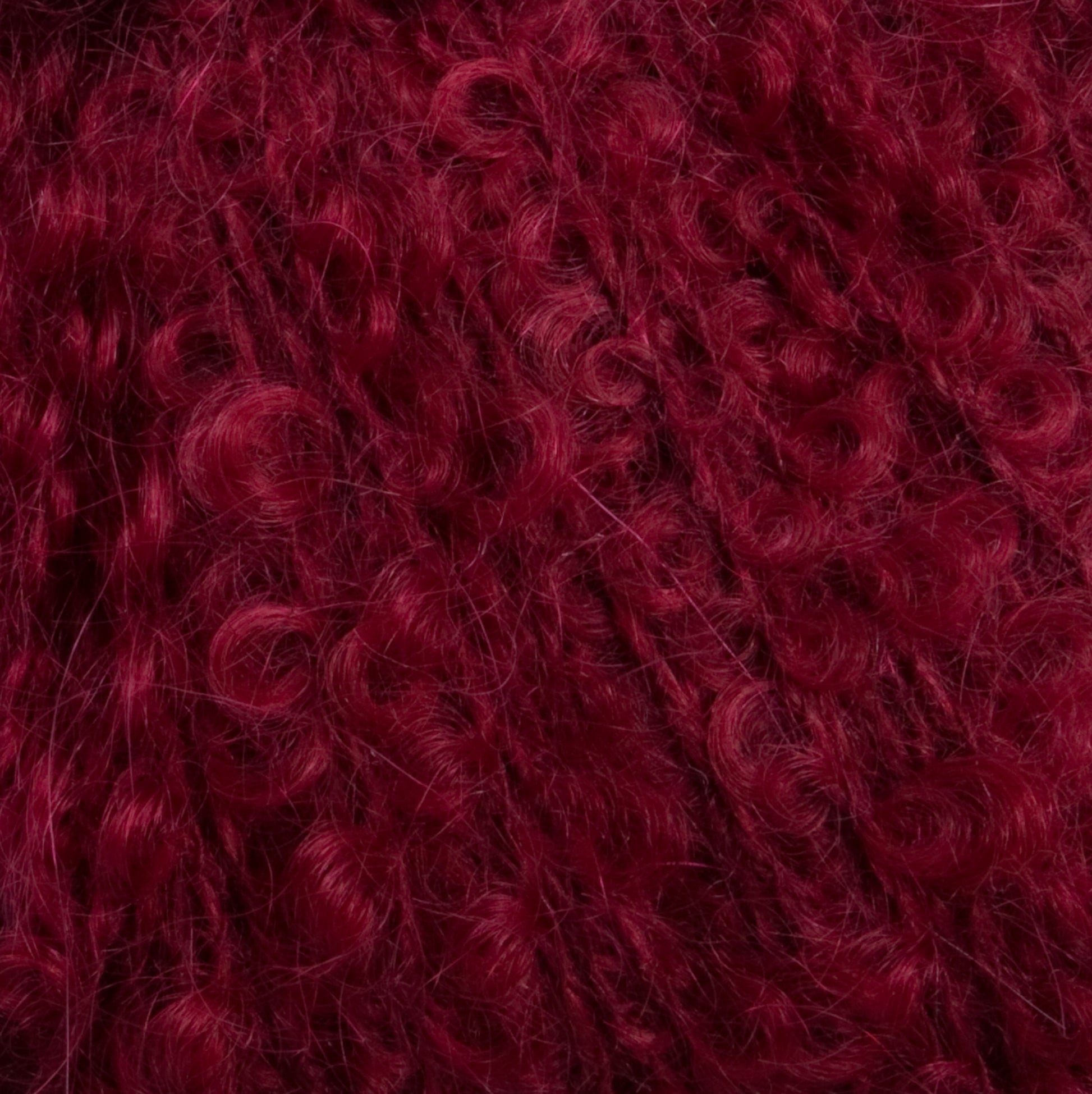 Close-up image of deep burgundy, tightly coiled, curly hair. The texture appears dense and voluminous, reflecting the luxurious appeal of Caledonian Dye Works' Victorian Bouclé Mohair Yarn. The richly colored curls are uniformly distributed and form a compact, intricate pattern with a slightly shiny appearance.