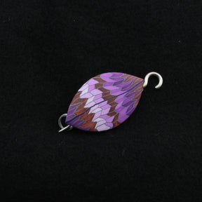 The Leaf Shawl Pin by Bonnie Bishoff Designs is marquise-shaped with a vivid mosaic pattern in shades of purple, red, and white set against a black background. This exquisite piece from Bonnie Bishoff features metal loops at each end for attaching to your shawl or other accessories, displaying intricate craftsmanship reminiscent of polymer clay design.