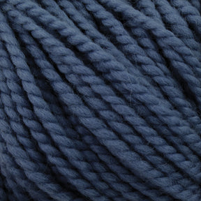 A close-up image of Norumbega yarn by Caledonian Dye Works showcases thick, twisted, dark blue Aran weight yarn. The texture is clearly visible, with individual fibers and strands tightly woven together, creating a dense and soft appearance. This durable fabric features 100% U.S. wool in a uniform, deep blue color.