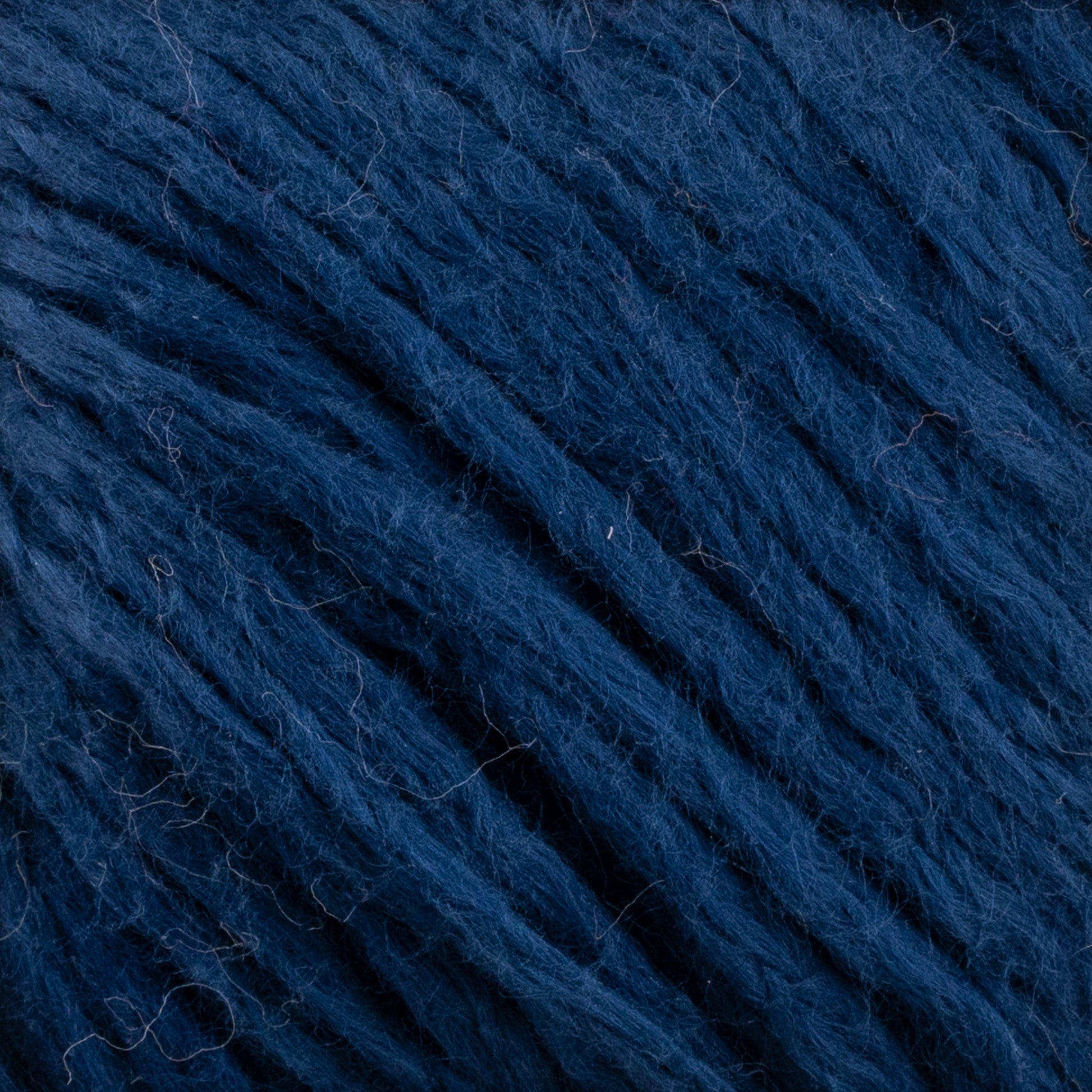 Close-up image of Cumulus Cotton by Juniper Moon Farm in a dark blue hue, showcasing its soft, fuzzy texture. The individual strands are clearly visible, intertwining to create a dense and tactile appearance. The rich, deep blue color of this yarn from Knitting Fever / Euro Yarns suggests a luxurious cotton material, perfect for weightless accessories that feel exquisitely gentle against the skin.