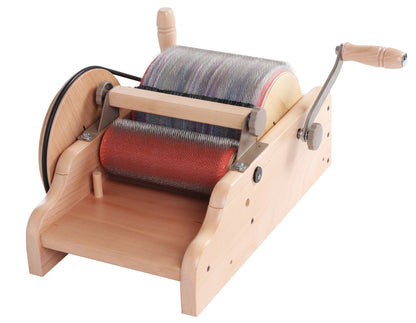 The Ashford Drum Carder - Super Fine 120 pts/in by Ashford Handicrafts Limited is displayed. It features a wooden hand-cranked design with metal teeth. The large drum is covered in bristles, accompanied by a smaller drum alongside it. There are two wooden handles: one for cranking and another smaller one likely for adjustments, both mounted on a wooden base.