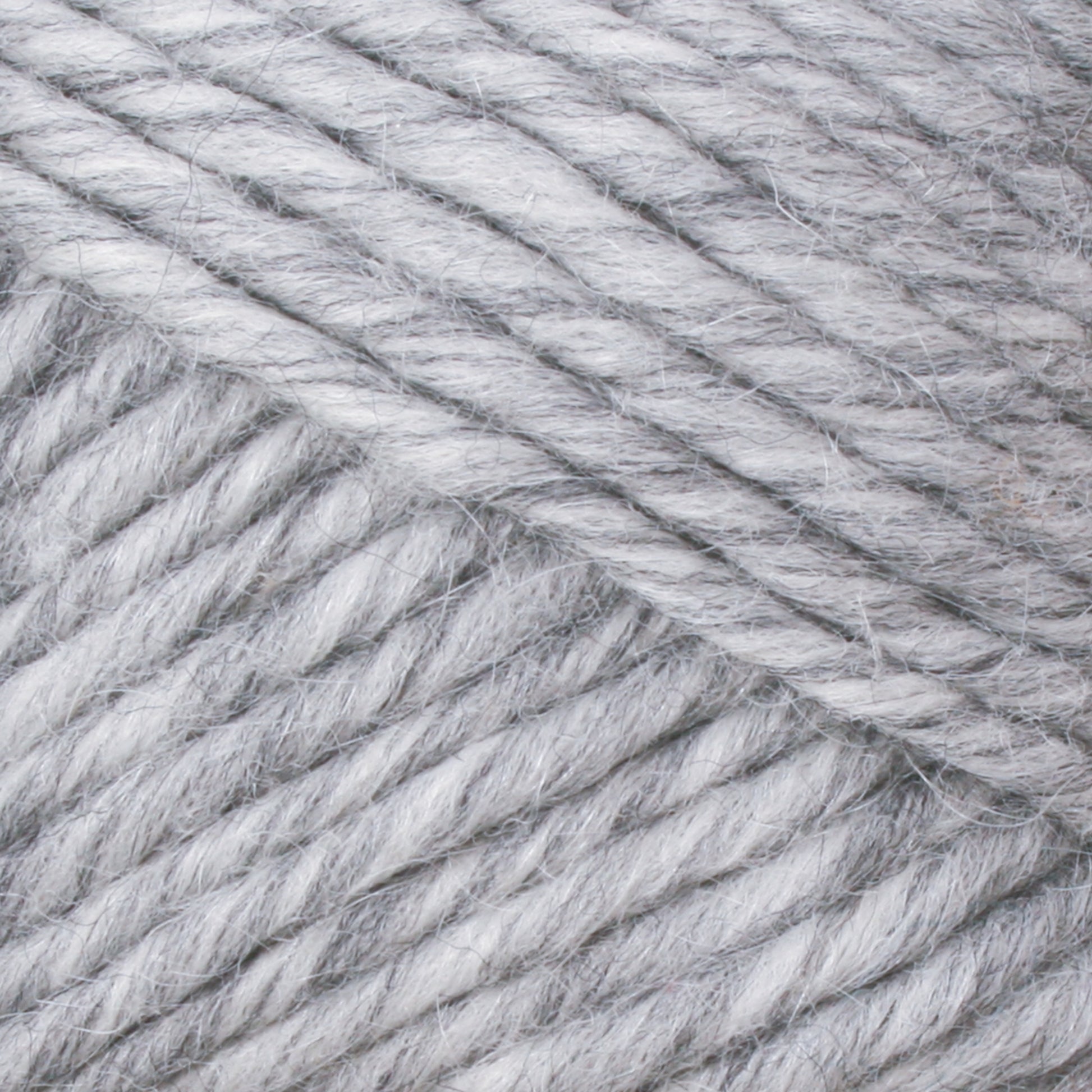 Close-up view of the soft, thick Lamb's Pride Bulky Yarn by Brown Sheep in shades of gray and white, twisted tightly in a ball. The texture appears plush and fibrous, making it ideal for knitting or crocheting cozy garments or accessories such as woven blankets or Icelandic sweaters. Perfect for dedicated knitters and crocheters.