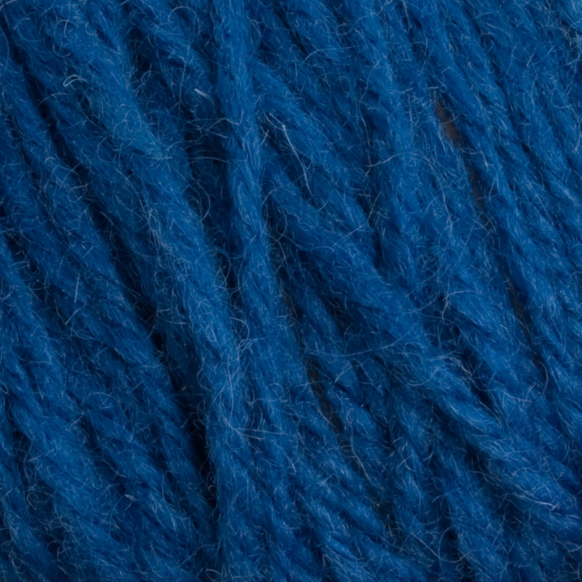 Close-up image of blue 100% Halcyon Deco Rug Wool fibers intertwined. The Caledonian Dye Works yarn has a slightly fuzzy texture with individual strands visible, giving it a rich, vibrant blue appearance. The image showcases the detailed and coarse texture of this versatile wool yarn.