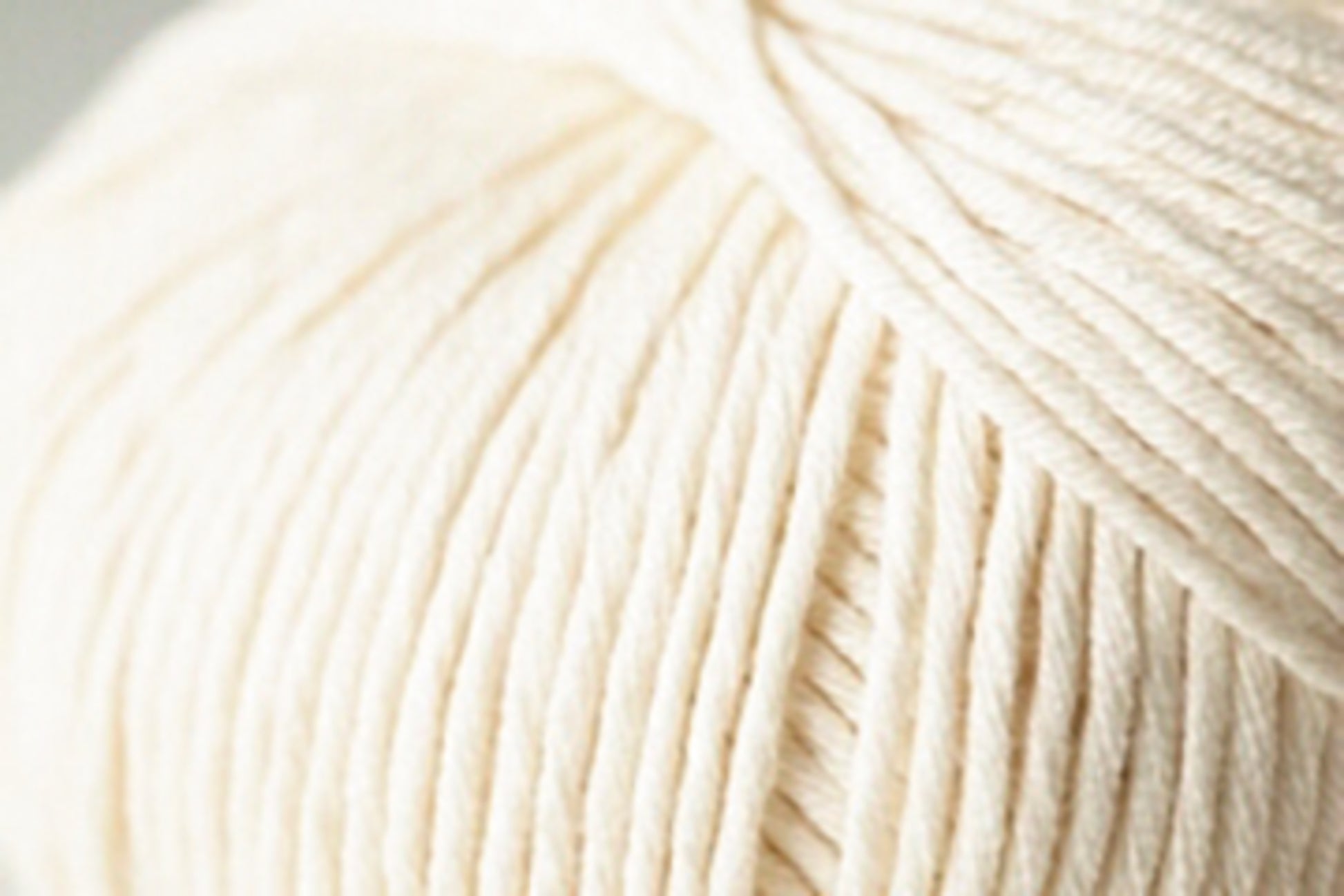 A close-up image of a cream-colored ball of Jo Sharp Soho Summer DK Cotton from Kingfisher Yarn & Fibre. The texture is smooth, with tightly wound strands visible, showcasing the yarn's softness and thickness—perfect for creating lightweight summer projects.