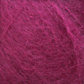 Close-up view of the Victorian Brushed Mohair Yarn | Large Skein by Caledonian Dye Works, showcasing its soft and wispy texture in a stunning magenta color. The fibers interlock in a random, intricate pattern, highlighting the material's fluffiness and vibrant hue.