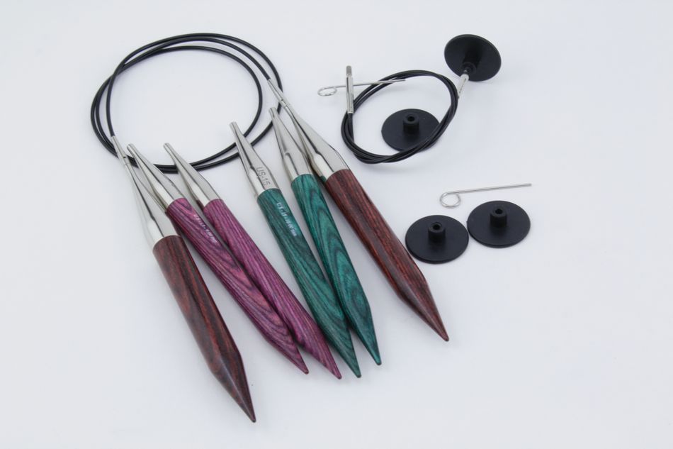 The Accessories Unlimited Dreamz Interchangeable Circular Knitting Needle Set features a vibrant array of colorful densified laminated birch tips in various shades of wood, two cables, two black stoppers, and a tightening key on a white background.