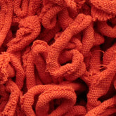 Close-up image of a textured, tangled mass of bright orange cotton loops from the Harrisville Potholder Loops - Traditional Size Mini Pack by Friendly Loom. The loops intertwine and overlap, creating a dense, intricate pattern reminiscent of those made on a traditional potholder loom.