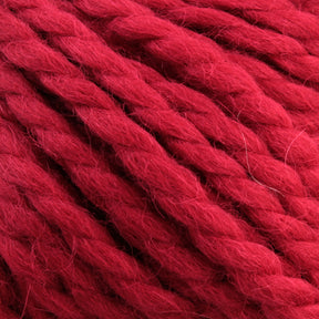 Close-up of thick, red Baby Alpaca Grande by Plymouth strands twisted together in a chunky texture. The ultra-soft fibers from Plymouth Yarn Co. are slightly fuzzy, giving the yarn a cozy and inviting appearance.