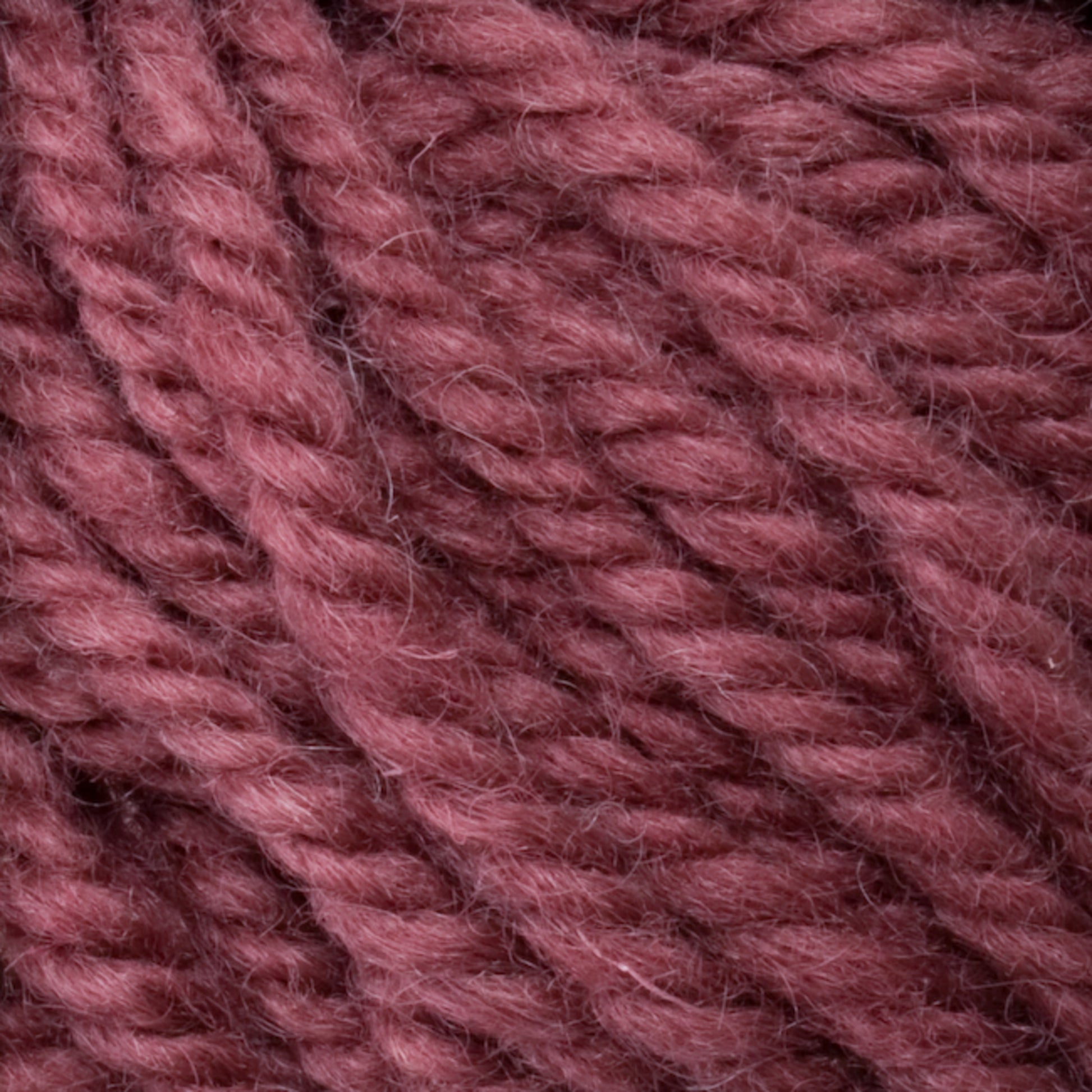 Close-up image of thick, tightly twisted Halcyon Yarn Classic Rug Wool from Caledonian Dye Works in a rich, dusty rose color. The texture appears soft and slightly fuzzy, crafted using hand-dye techniques to ensure a cozy and warm material suitable for knitting or crocheting projects. Ideal for rug weavers seeking excellence.