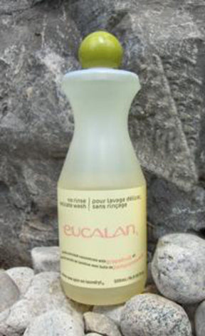 A 16.9 oz bottle of Eucalan Wool Wash, enriched with lanolin, is placed on a rocky surface. The translucent bottle contains a yellowish solution and features a green round cap and beige labeling in both English and French. This 100% biodegradable concentrate from Eucalan promises gentle care for your finest fabrics.