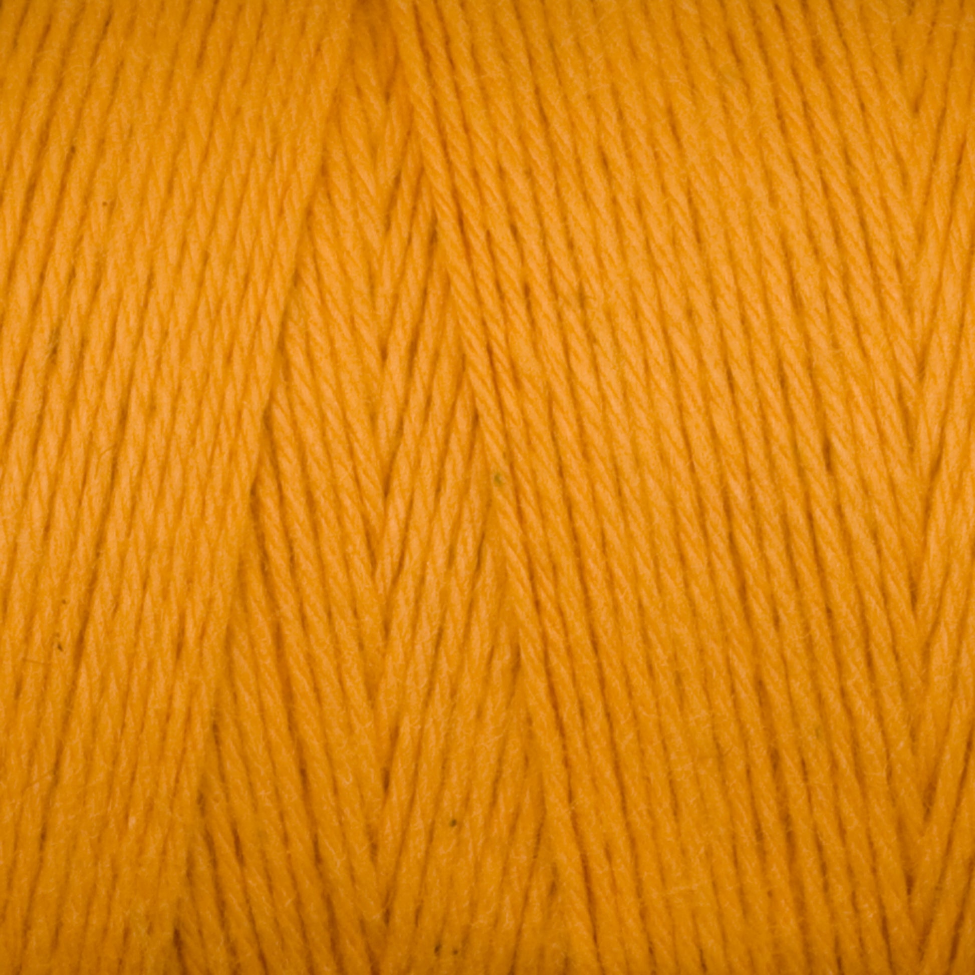 Close-up image of Maurice Brassard's Cotton 8/8 Carpet Warp in a bright orange color. The strands are tightly wound together, showcasing their smooth texture and slight sheen. The vibrant hue and detailed fibers of the unmercerized cotton yarn are clearly visible, making it perfect for knitting and crochet projects.