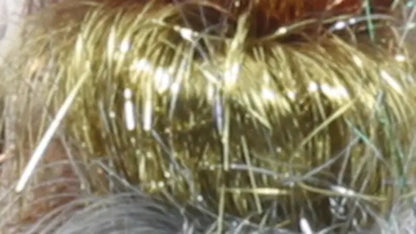 A close-up image featuring shiny strands of Crystal Mylar Fiber from Foxglove Fiberarts Supply in metallic gold and silver, intertwined to create a decorative texture. The tinsel reflects light with shimmering highlights, giving it a glimmering and festive appearance. Now available on clearance!