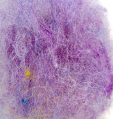 A close-up image of a dryer lint trap's contents, showing a tangled mesh of fibers reminiscent of Harrisville Designs' Harrisville Dyed & Carded Wool Fiber. The lint is predominantly purple with hints of white, blue, and yellow threads throughout, creating heathered colors. The texture appears soft and fluffy.