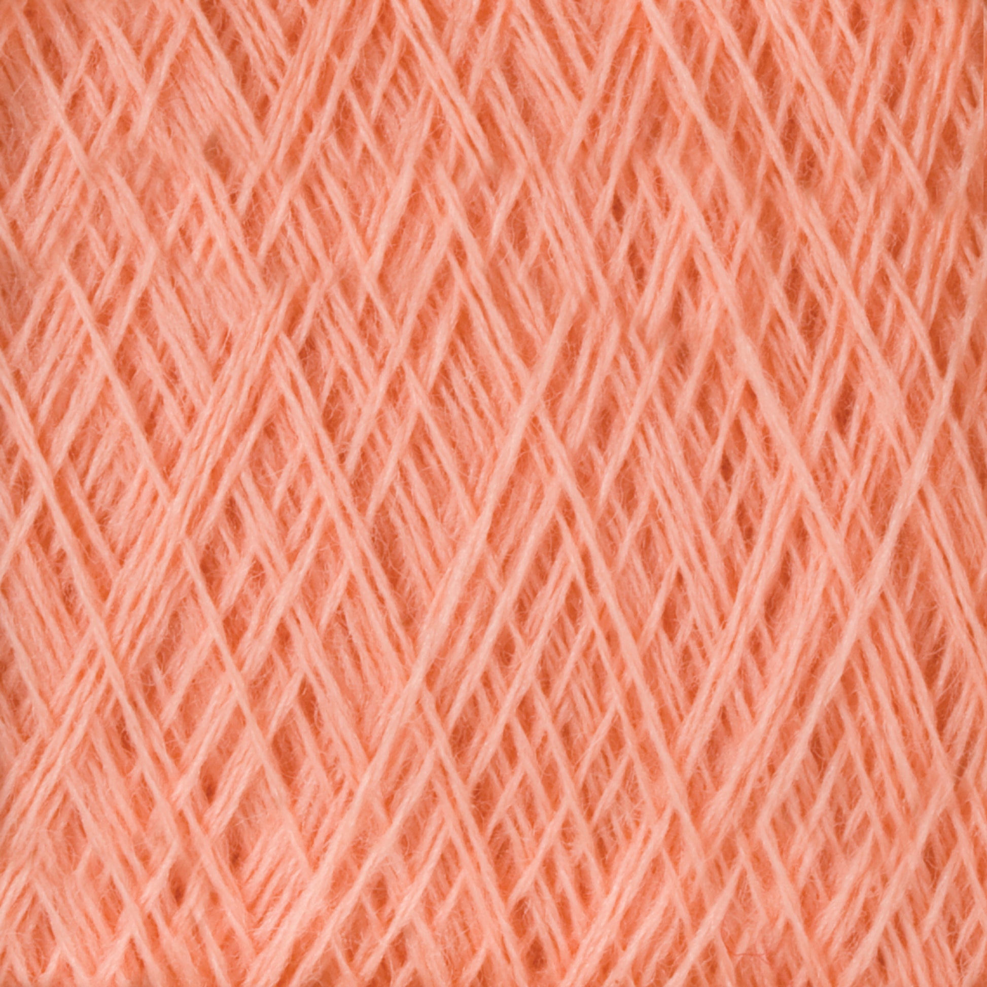 Close-up image of tightly wound, soft, peach-colored Jagger Brothers, Inc. JaggerSpun Maine Line 3/8 Yarn on a large cone. The strands intersect diagonally, creating a geometric pattern. The texture appears fluffy and fibrous, with a warm, inviting hue characteristic of soft medium-grade wool.