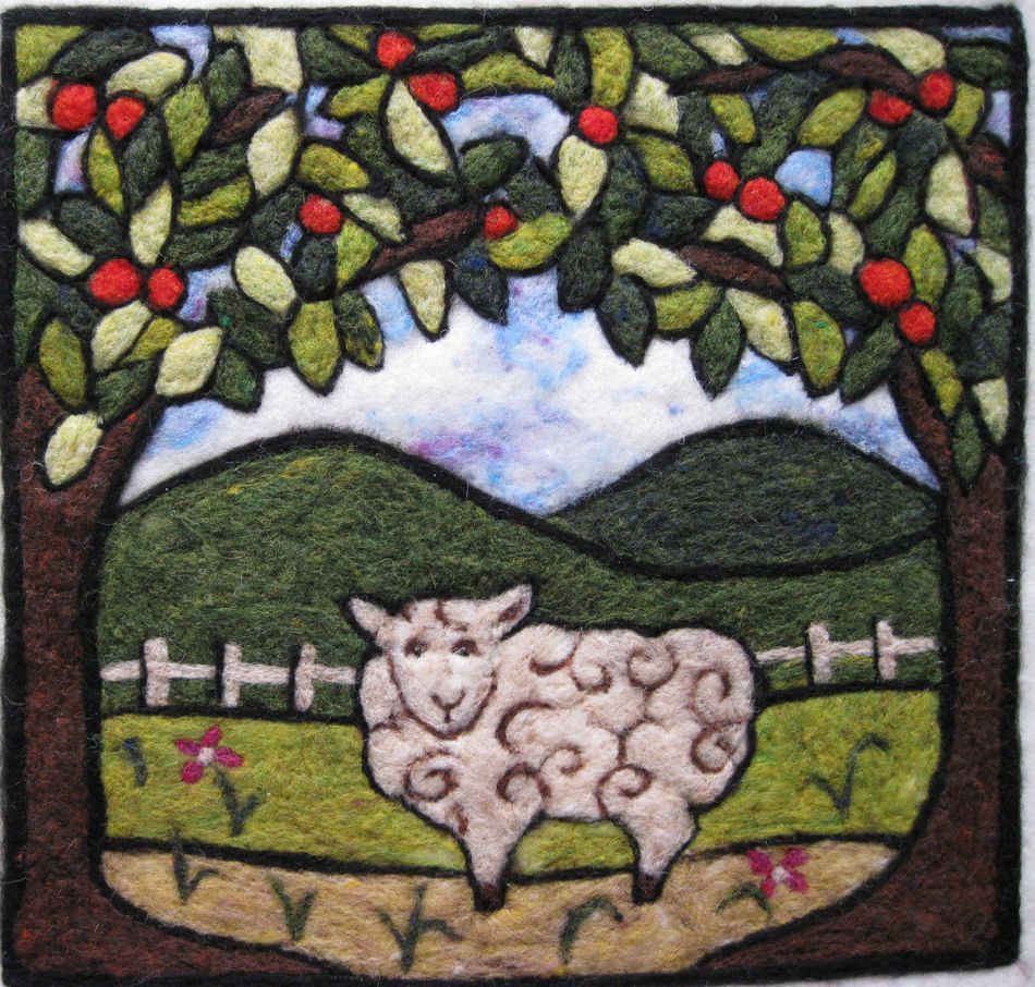 The Felting Studio's Needle Felting Tapestry Kit allows you to create a charming wool felt artwork. The scene depicts a cheerful sheep standing on grassy terrain, framed by two trees bearing red fruit. Behind the sheep, a white fence and rolling green hills stretch under a blue sky. Red flowers dot the ground near the sheep, completing this picturesque wool tapestry.