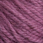 A close-up image of a skein of Halcyon Yarn Classic Rug Wool from Caledonian Dye Works in a dusty rose color. The soft fibers are tightly twisted together, creating a textured and cozy appearance. The hand-dye process gives the yarn a slightly fuzzy look, and the color is a muted, warm shade of pink favored by weavers.