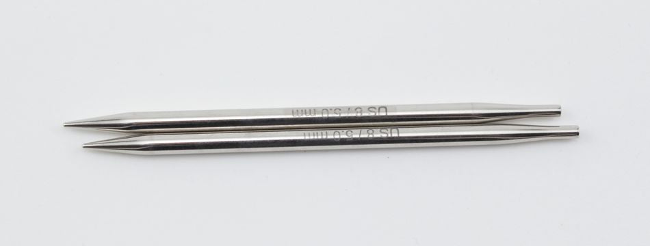 A pair of Accessories Unlimited Nova Platina Interchangeable Knitting Needles, 4.5" Tip, lying parallel on a white background. Each needle, resembling hollow brass pipes, has tapered tips at both ends and engraved text near the middle.