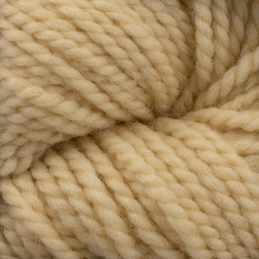 Close-up of a skein of thick, cream-colored Aran weight Norumbega yarn from Caledonian Dye Works, showing the detailed texture and tightly twisted fibers. Made from 100% U.S. wool, the yarn appears soft yet forms a durable fabric suitable for knitting or crocheting warm garments.