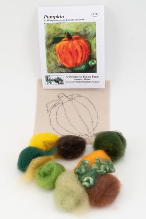 The Thyme Tile Felting Kit (no tools) from A Wrinkle in Thyme Farm is perfect for beginner felters, featuring a small card with a pumpkin illustration, a partially completed wool outline of a pumpkin on fabric, and various colors of wool roving, including shades of green, yellow, brown, and orange, arranged neatly below the fabric.