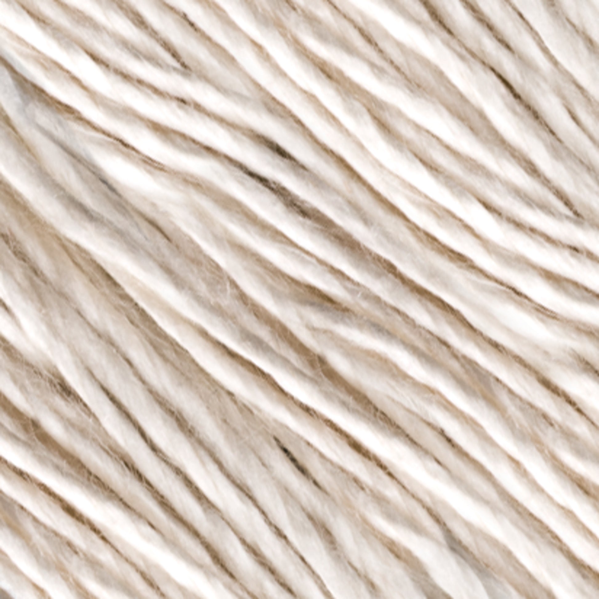 The close-up image showcases strands of Henry's Attic Soft Twist Natural Silk Yarn. This yarn consists of twisted natural fibers, appearing soft and slightly uneven in thickness, creating a textured background. The colors range from off-white to pale beige, giving it a natural and organic look perfect for hand washing.