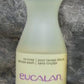 A 16.9 oz bottle of "Eucalan Wool Wash" with a lavender scent is placed against a stone background. This lanolin-enriched concentrate is translucent white with a green cap and purple text. Labeled in both English and French, it boasts a 500ml capacity and is 100% biodegradable.