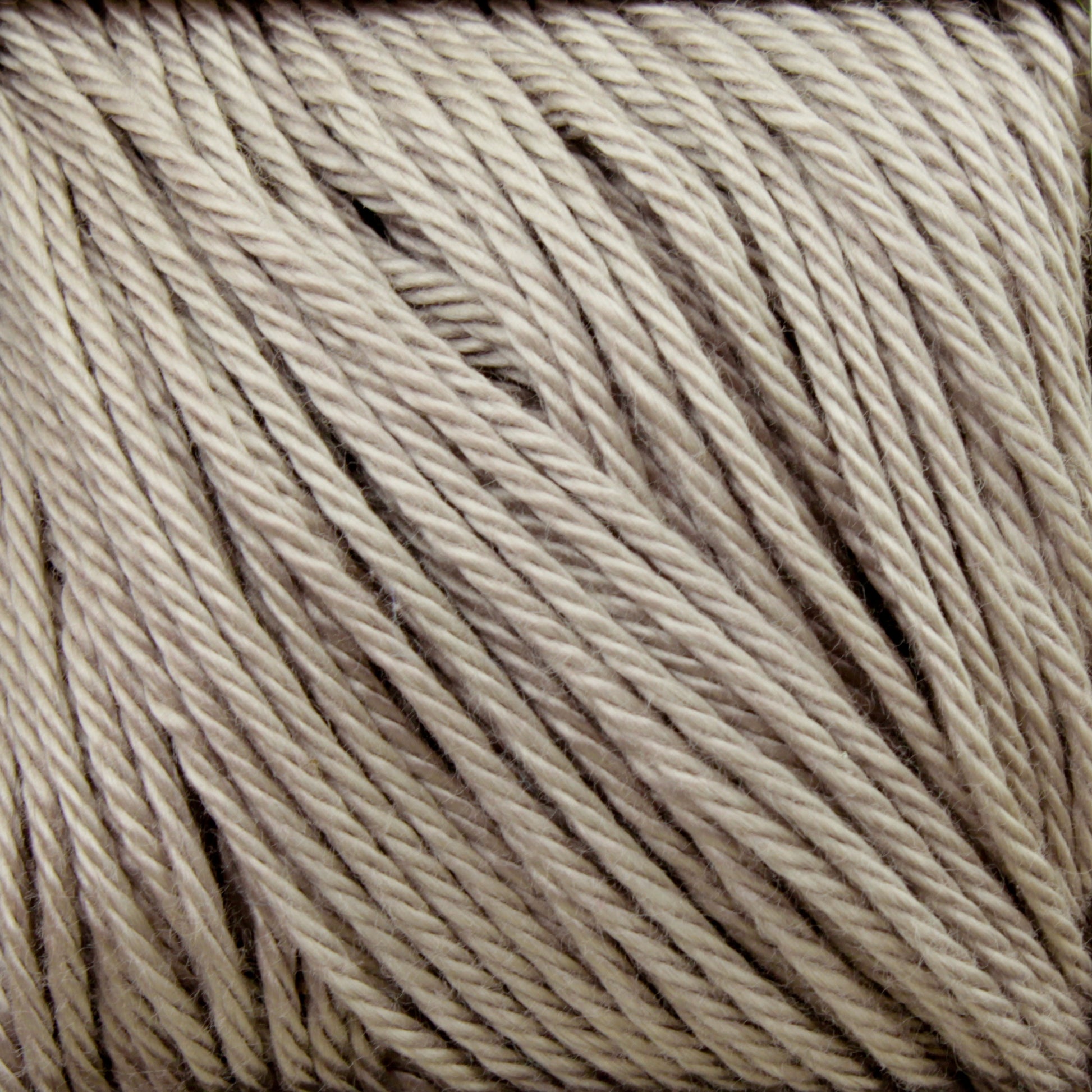 Close-up of beige Cascade Ultra Pima Cotton Yarn twisted into strands and neatly arranged in parallel rows. The Cascade Yarns product, made from Peruvian Pima Cotton, has a soft, slightly fluffy texture and a neutral color, making it suitable for various knitting or crocheting projects. The background is also beige, blending with the yarn.