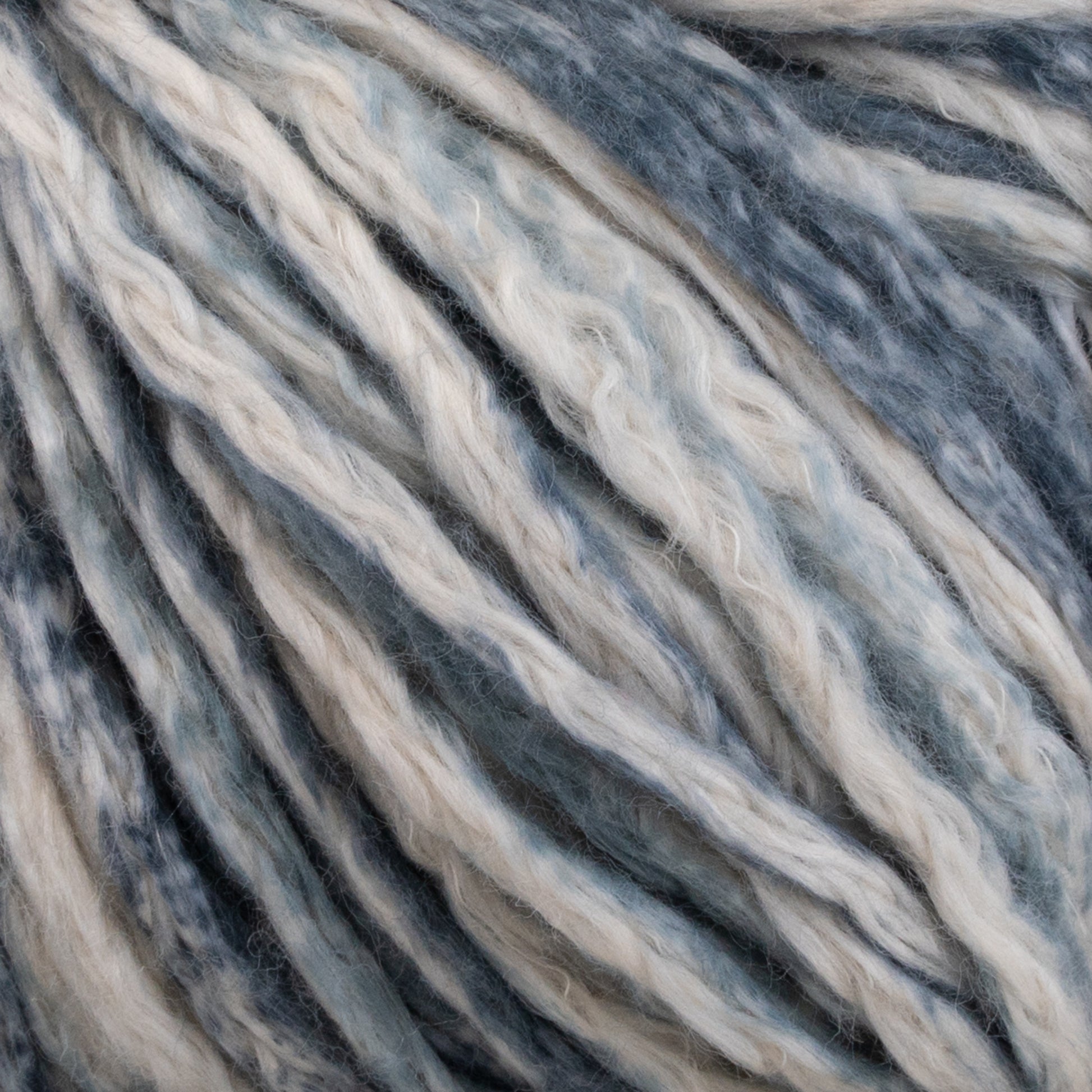 Close-up of Cumulus Cotton by Juniper Moon Farm in shades of blue, gray, and white. The thick strands are twisted together, highlighting the texture and variations in color. The image emphasizes the fibrous and soft nature of the durable chainette construction by Knitting Fever / Euro Yarns.