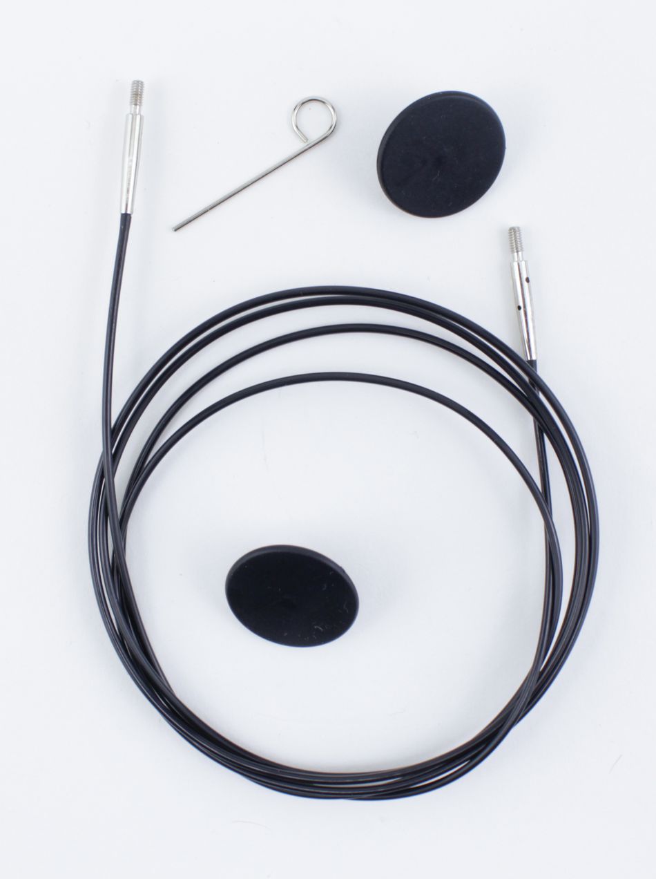 The image showcases the Accessories Unlimited Interchangeable Circular Needle Cord for Dreamz and Nova, featuring a black circular cable with metal connectors at both ends, resembling knitting accessories. Also included are a small black rubber cap, a pin with a loop at the top, and an oval black rubber plug, all set against a white background.