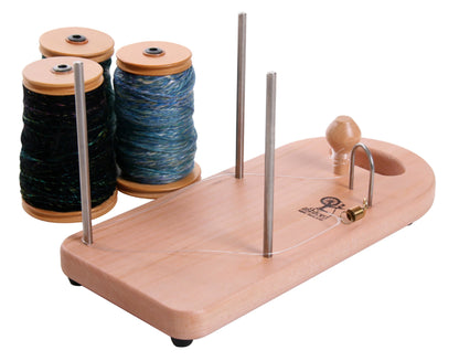 The Ashford Lazy Kate, by Ashford Handicrafts Limited, is pictured with three spools of multicolored thread placed on wooden bobbins. The holder features metal rods and a small wooden knob at one end and is designed to organize and manage thread during sewing or crafting activities.