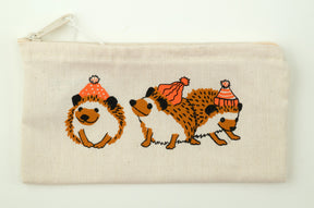 Introducing the Wee Hedgehog Zip Pouch by Mum n Sun Ink, crafted by Bonnie Bishoff. This cream-colored zippered pouch is made from Envirotote canvas and features three charming hedgehog illustrations. The left hedgehog is curled into a ball, the middle one is standing, and the right one is walking away—all adorned with red and white winter hats. Perfect for storing shawl pins or small essentials.