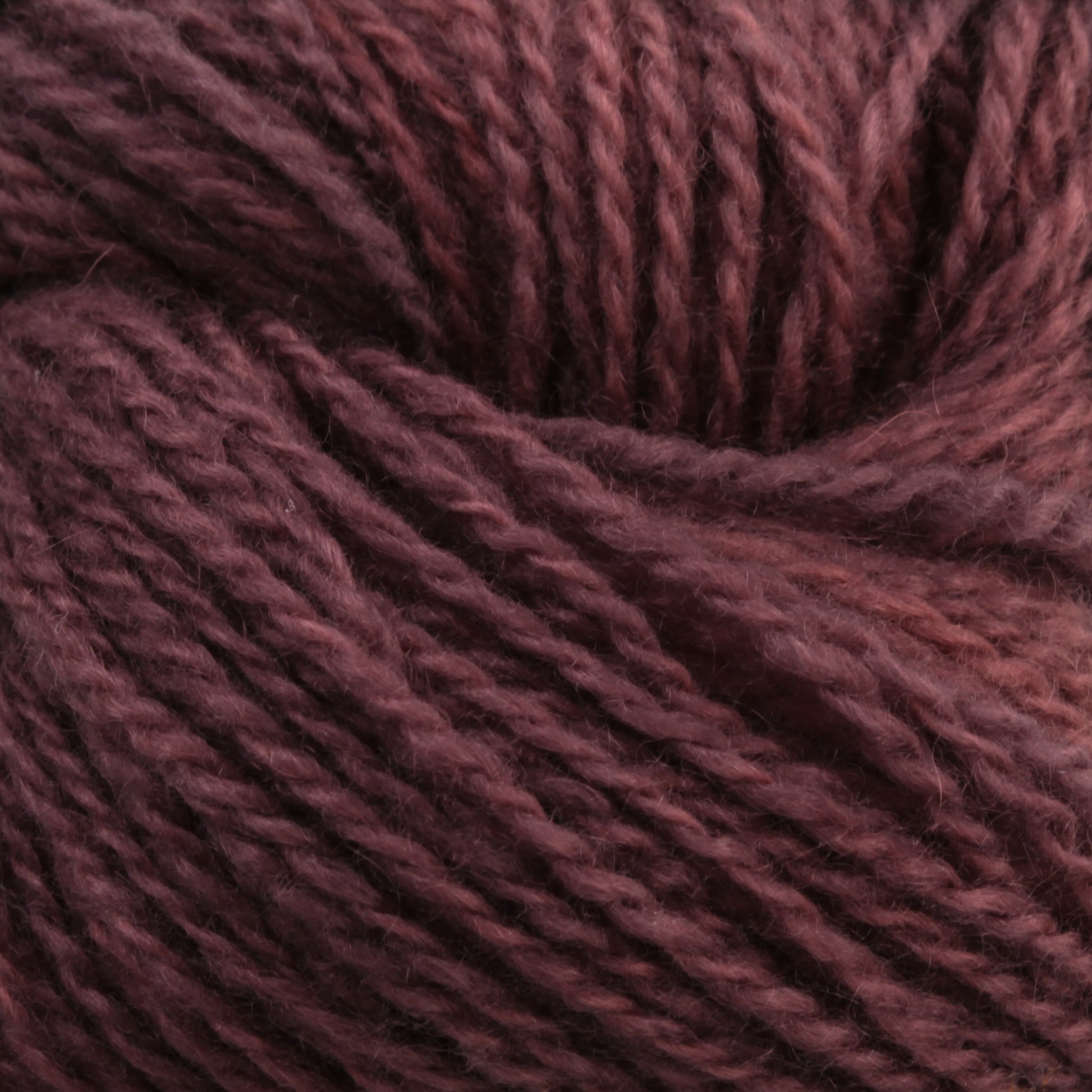 Close-up of a ball of Jade Sapphire Cashmere 2-Ply yarn by Jade Sapphire Exotic Fibres. The dark reddish-brown fibers are twisted together, showcasing a soft and woolly texture. This hand-dyed color emphasizes the rich tones and detailed strands, perfect for finely knit sweaters or woven accessories.