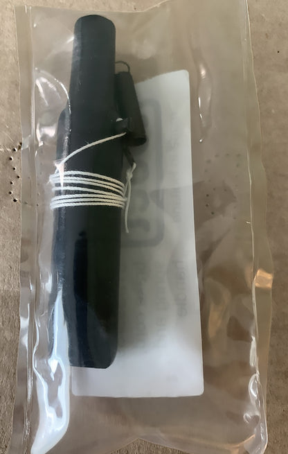 A black cylindrical object wrapped with a thin white cord is enclosed in a clear plastic pouch, resembling an accessory for a Louët wheel. A partially visible piece of white paper with text is beneath the object inside the pouch, indicating it as the Louët S11/S95/S96 brake cord and parts from Louët Inc.