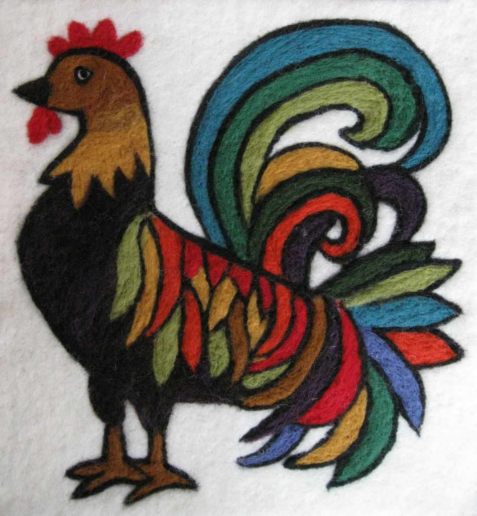 A vibrant, stylized rooster is depicted in felt art, crafted from The Felting Studio's Needle Felting Tapestry Kit. The rooster features a black body with multicolored feathers, including shades of green, red, yellow, and blue. Its tail feathers are especially elaborate and colorful, standing out against the white background.