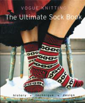 The cover of "The Ultimate Sock Book" by Soho Publishing showcases a close-up of two sock-clad feet resting on a stool. The socks feature a red, white, and black geometric pattern. Perfect for beginners, the book's text "history • technique • design" is prominently displayed at the bottom of the cover.