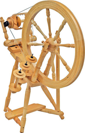 The Kromski Interlude Spinning Wheel by Kromski North America, featuring a single drive angle treadle design, boasts a large wheel on the right side connected to several smaller spindles and components on the left. Crafted from European alder and birch, its frame showcases intricate woodworking details.