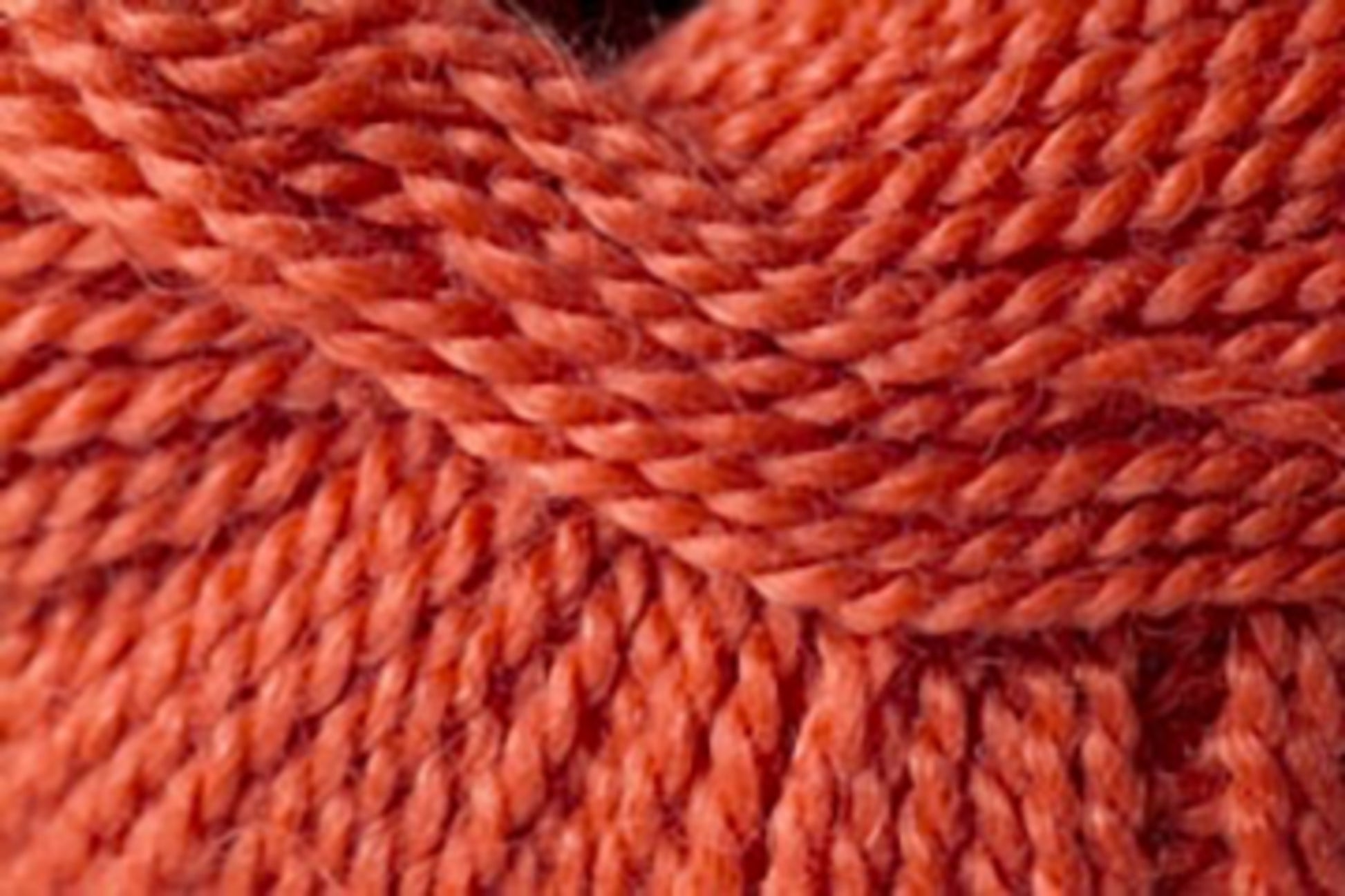 Close-up of a deeply textured, twisted strand of rust-colored Jo Sharp Alpaca Kid Lustre by Kingfisher Yarn & Fibre. The image highlights the tightly woven fibers, showcasing the yarn's thickness and vibrant hue.