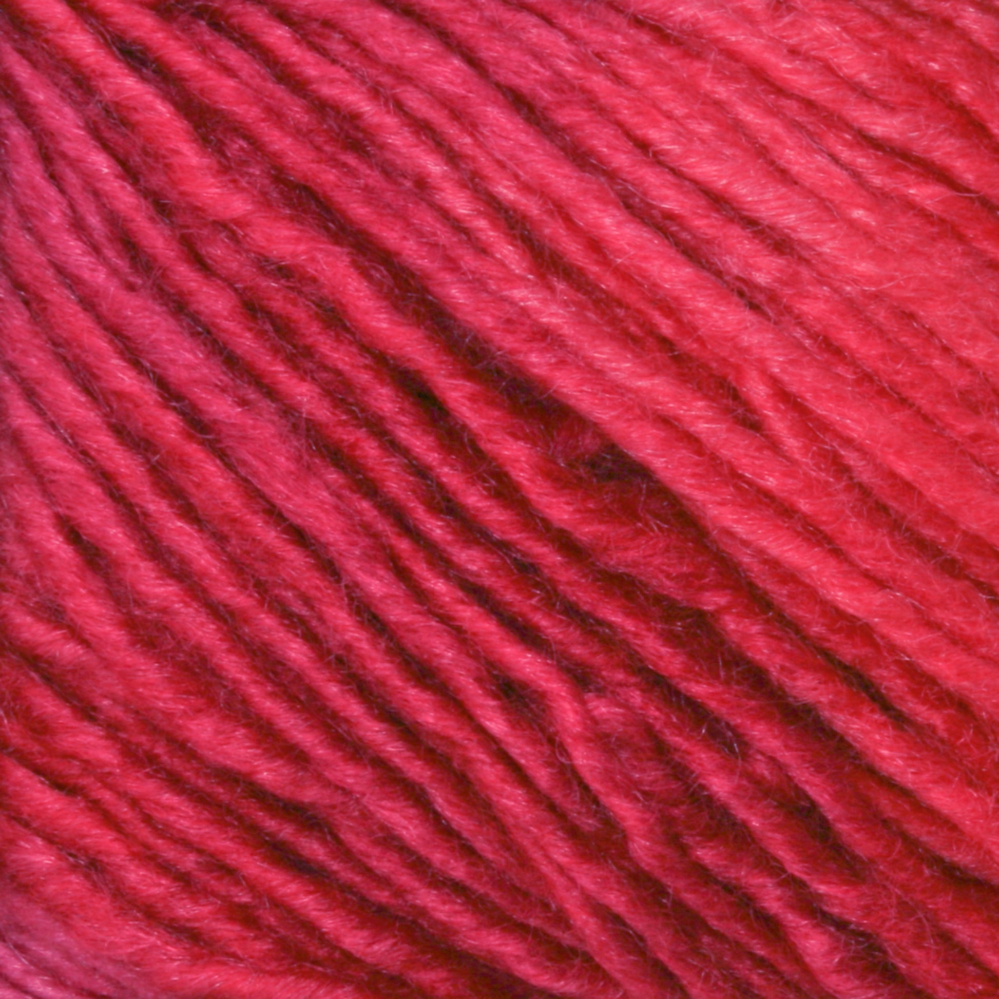 Close-up of Malabrigo Silky Merino by Malabrigo Yarn in red, showcasing the soft, textured strands tightly wound together. The yarn appears to have a slight sheen, highlighting the individual threads and their natural variations in thickness and color.