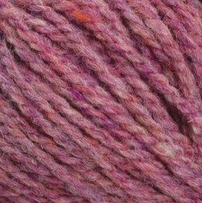 A close-up image of Harrisville Designs' Harrisville Shetland Yarn - Unwashed Cones, which is perfect for lightweight blankets. The yarn showcases beautiful shades of pink, purple, and occasional hints of orange and white, creating a textured and intertwined pattern reminiscent of Fair Isle knitting designs. The fibers appear soft and slightly fuzzy.