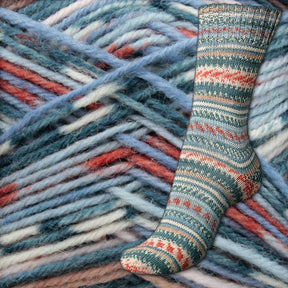 A vibrant Fair Isle sock from the Regia 4-ply Design Line by Arne & Carlos is showcased against a backdrop of thick, multicolored yarn in hues of blue, teal, and coral. The yarn criss-crosses in various directions, providing a textured setting for the sock. This striking display highlights the expertise of Sirdar - Regia, Schachenmayr & Rowan brands.