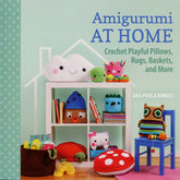 A book cover titled "Amigurumi At Home" by Ana Paula Rímoli, published by Martingale & Co, displays a shelf filled with vibrant crocheted home decor items. The cheerful designs include a smiling cloud, whimsical houses, an owl, and even a chair featuring a blue owl-shaped pillow.