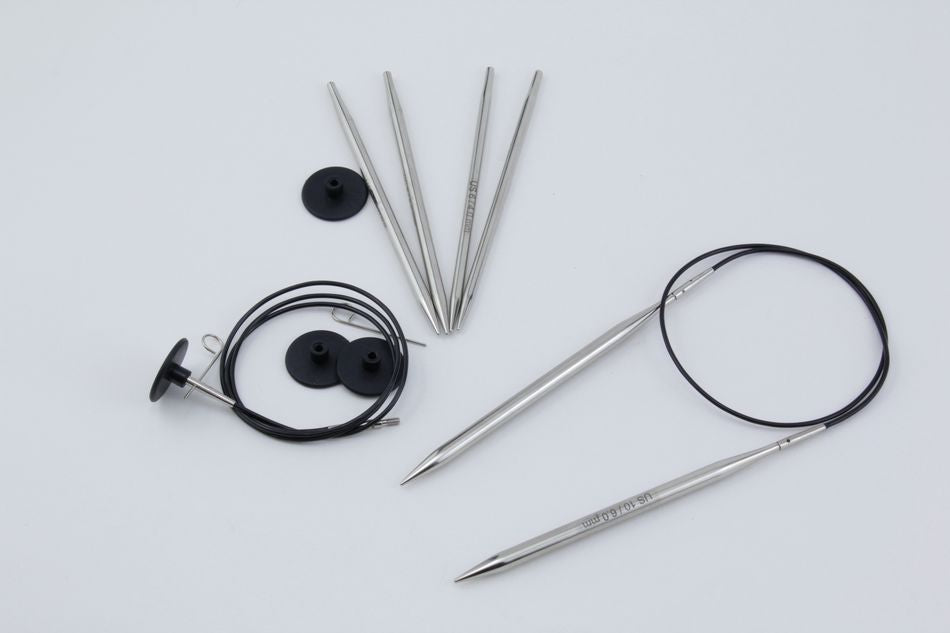 A meticulously designed Nova Platina Interchangeable Circular Knitting Needle Set from Accessories Unlimited, featuring multiple metal needle tips, circular needle cables, and black cable stoppers, arranged on a plain white surface.