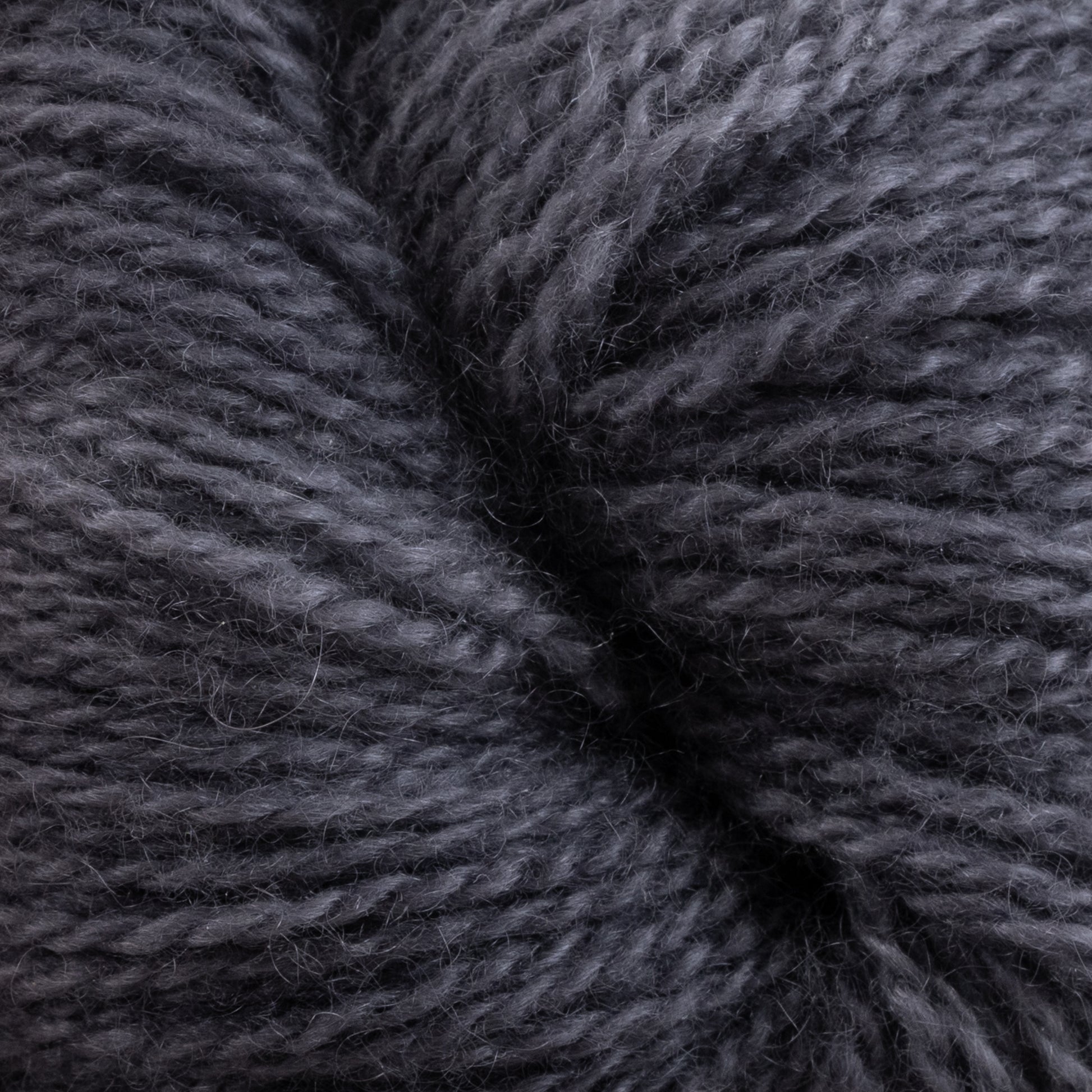 Close-up of Jade Sapphire Cashmere 2-Ply yarn by Jade Sapphire Exotic Fibres. The texture appears soft and slightly fuzzy, with tightly wound fibers. The yarn has a consistent dark gray color and a fluffy appearance, suggesting it is suitable for cozy knitting projects like finely knit sweaters or scarves.