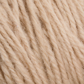 Close-up image of Halcyon Deco Rug Wool by Caledonian Dye Works in a beige hue. The soft, twisted fibers are tightly packed, showcasing the texture and detail of the material. The strands appear thick and slightly fuzzy, indicating a potential use for knitting or crocheting versatile yarn projects.