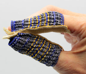 Two fingers are shown wearing *Leather Finger Guards, Open-End* from Magid Glove & Safety Co LLC, featuring colorful, hand-woven patterns in shades of blue, yellow, and white. These fabric protectors come with a leather backing and are perfect for sewing or quilting enthusiasts. The fingers are held close together against a plain grey background.