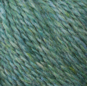 Close-up image of Harrisville Designs' Peace Fleece Yarn in a green and blue variegated pattern with a soft, fluffy texture. The fibers appear twisted together, creating a cohesive bundle. This worsted weight knitting yarn showcases subtle highlights of various shades of green and blue throughout.