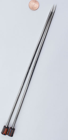 A set of two Nova Platina Single Point Knitting Needles by Accessories Unlimited, featuring silver-colored metal shafts and dark wooden tips, is positioned on a light surface with a penny placed near the top for size comparison.