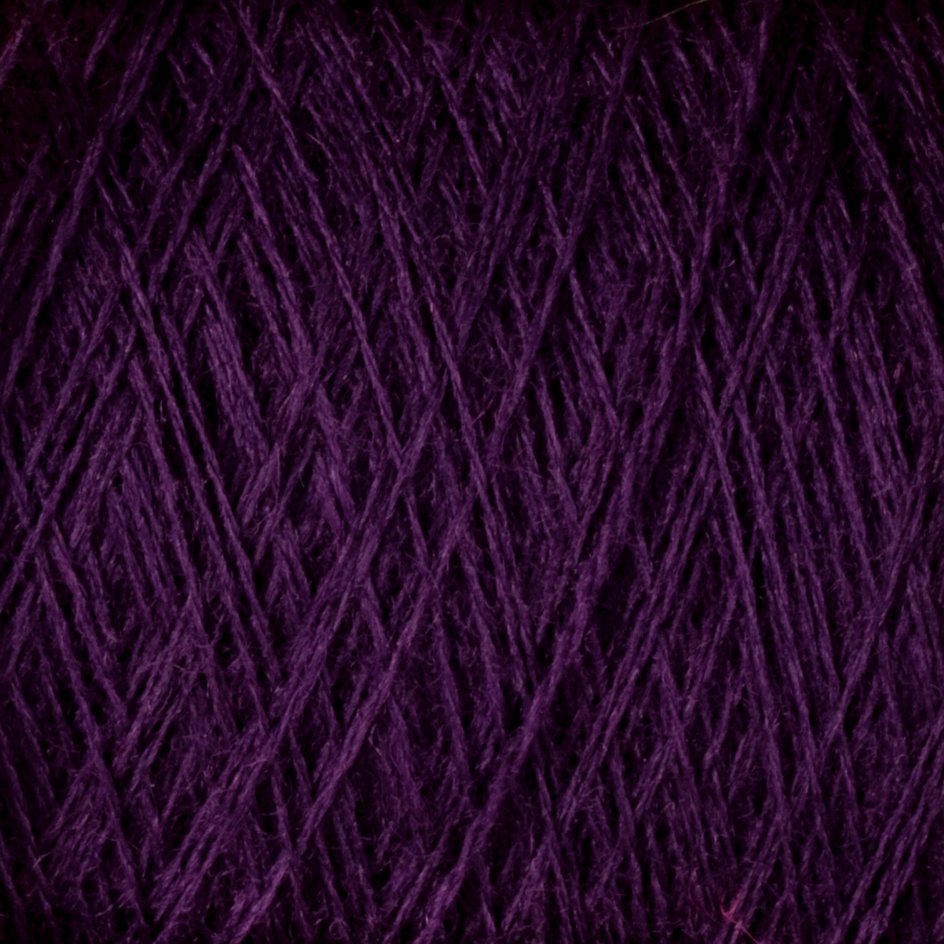 Close-up image of a bundle of dark purple JaggerSpun Maine Line 3/8 Yarn | Mini-cone from Jagger Brothers, Inc., showcasing the texture and intertwined strands typical of Maine wool yarns. The dense, fibrous pattern reveals rich, deep colors with threads overlapping in various directions.