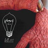 Close-up of a person wearing red knitted fingerless gloves, holding their arm. The text reads "Filament No. 4" inside a light bulb outline and "Fall 2017 Knit Filament" below. A stylish addition to women's garments featured in Knit Filament's quarterly publication.