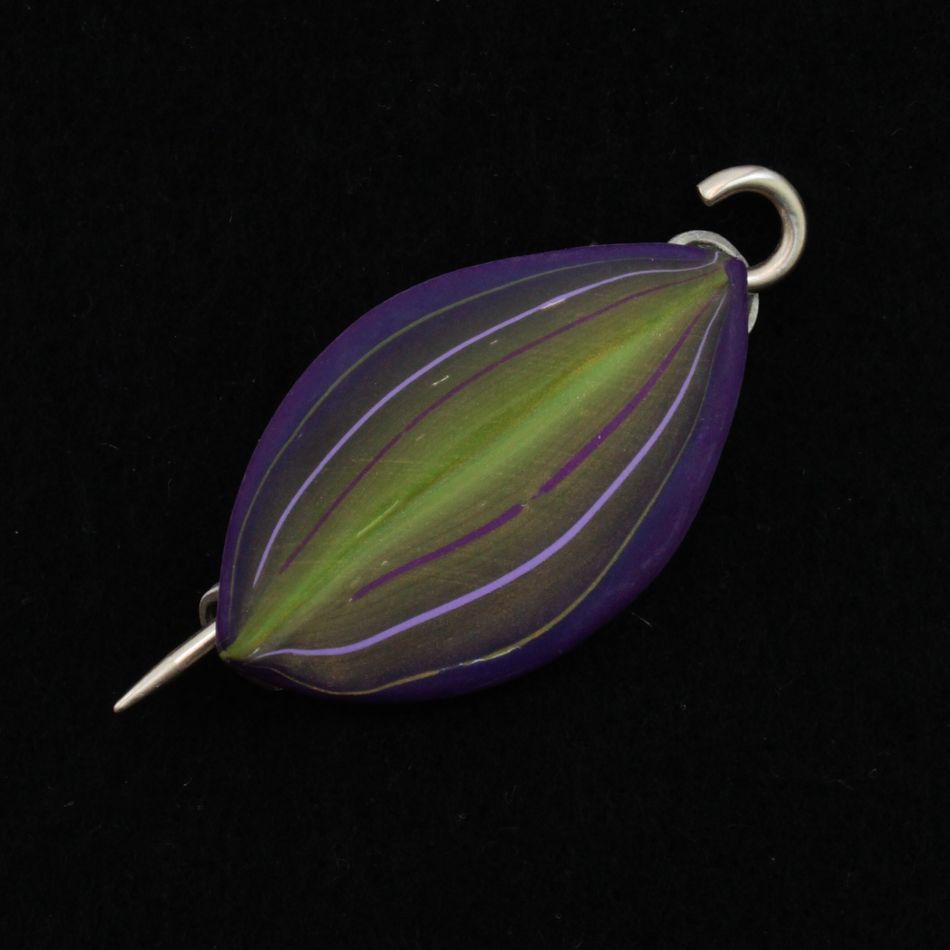 A single Hosta Shawl Pin, designed by Bonnie Bishoff, resembling a detailed leaf with a polymer clay construction featuring a green center and dark purple edges. Light purple veins extend from the center to the edges. The pin comes with a small, silver hook at the top for attaching. The background is solid black.